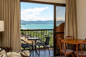 Een balkon met een tafel en stoelen, uitzicht op zee en bergen, en een schuifdeur.
