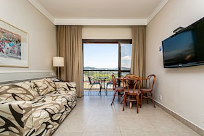 Habitació d'hotel amb sofà, televisió, balcó amb taula i cadires i un quadre a la paret.