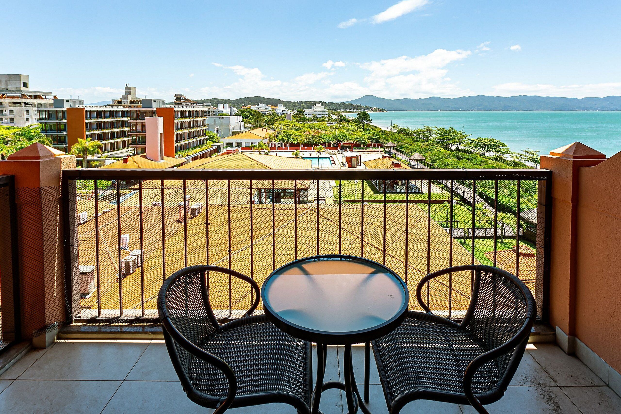 A balcony with a table and chairs, overlooking a pool and buildings.