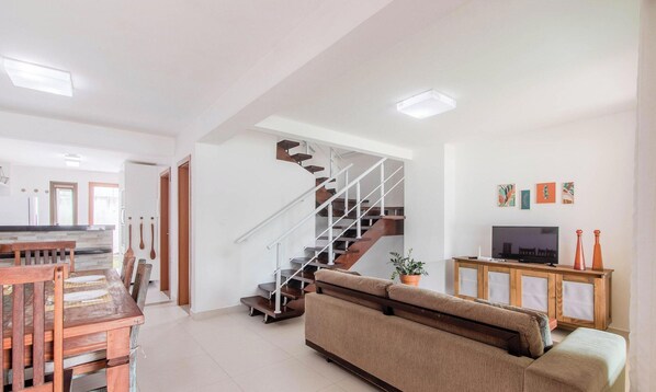 Uma sala de estar moderna com escada, sofá, mesa de jantar e televisão.
