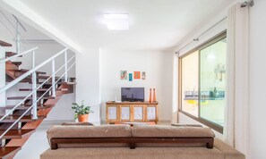 Una sala de estar moderna con una escalera de madera, un televisor de pantalla plana sobre un mueble de madera y un ventanal con vistas al exterior.