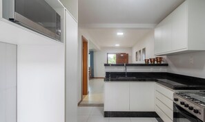 A modern kitchen with white cabinets, a black countertop, and a gas stove. - House in Cond. W/pool, 500 m From the Sea Atp0001 (Porto Seguro)