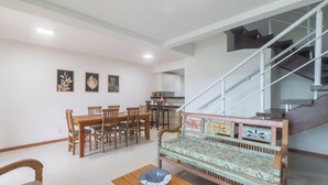 A dining area with wooden furniture, a sofa with a patterned cover, and a staircase with metal railings.