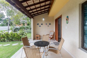 A covered patio with wicker chairs, a small table, and decorative plates on the wall. - House in Cond. W/pool, 500 m From the Sea Atp0001 (Porto Seguro)