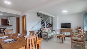 A modern living room with a dining area, a staircase, a television, and a kitchen visible in the background. - House in Cond. W/pool, 500 m From the Sea Atp0001 (Porto Seguro)