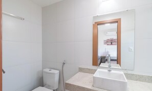 A bathroom with white tiles, a toilet, a shower, and a sink with a mirror above. - House in Cond. W/pool, 500 m From the Sea Atp0001 (Porto Seguro)