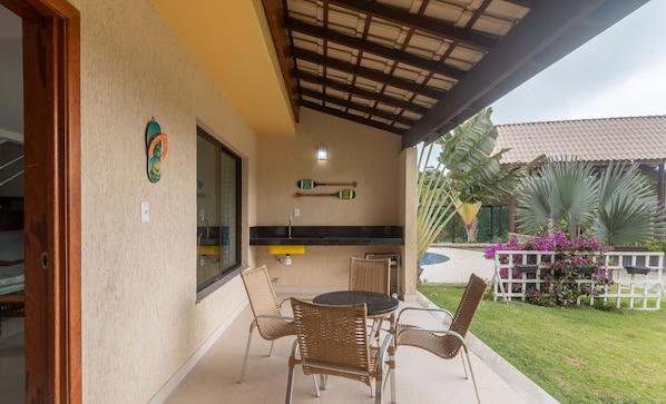 A covered patio with wicker furniture, a small table, and a window with a view of the garden.