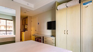 Ein Hotelzimmer mit einem Bett, einem Schreibtisch mit Stuhl, einem Fernseher und einem Kleiderschrank.