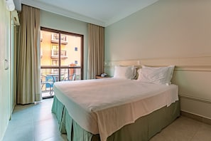 A hotel room with a large bed, a window with curtains, a balcony, and a view of buildings. - Comfort in Spectacular Luxury Resort Jbv106 (Florianópolis)