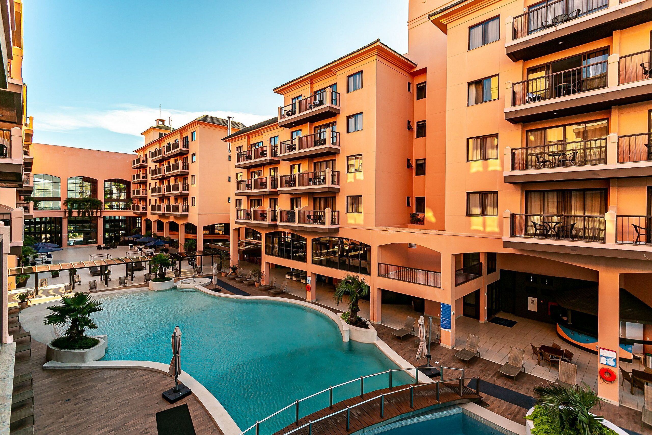 A multi-story hotel with a central swimming pool, outdoor seating areas, and balconies on each floor.