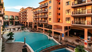 Ein mehrstöckiges Hotel mit einem zentralen Schwimmbecken, Sitzbereichen im Freien und Balkonen auf jeder Etage.
