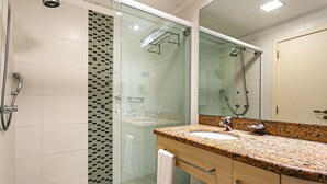Un baño moderno con ducha envuelta en vidrio, lavamanos de granito y un espejo grande.