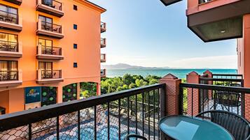 Uma varanda com mesa e cadeiras de vidro, com vista para uma piscina e para o mar e as montanhas.