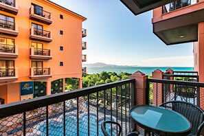 Uma varanda com mesa e cadeiras de vidro, com vista para uma piscina e para o mar e as montanhas.