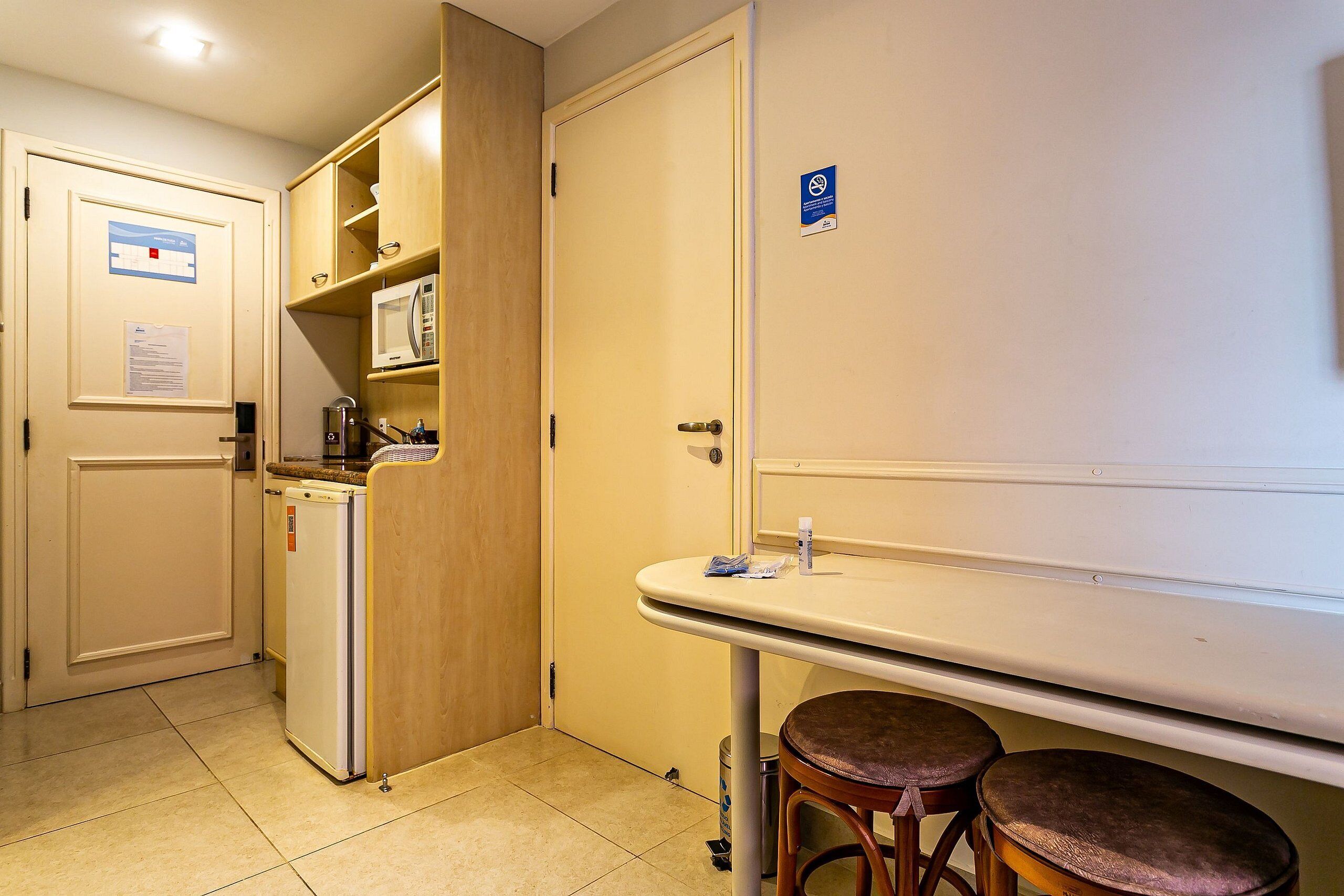 A compact kitchen with a microwave, a small refrigerator, and a sink with stools.
