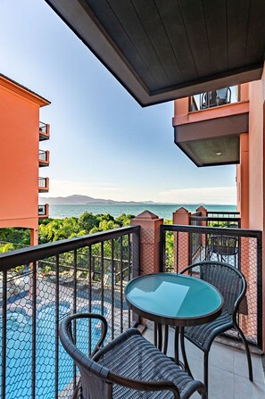 Uma varanda com mesa de vidro e cadeiras de vime, com vista para uma piscina e uma paisagem deslumbrante do mar e das montanhas.