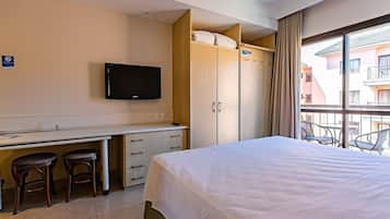 Una habitación de hotel con cama, escritorio con dos taburetes, televisor y armario.