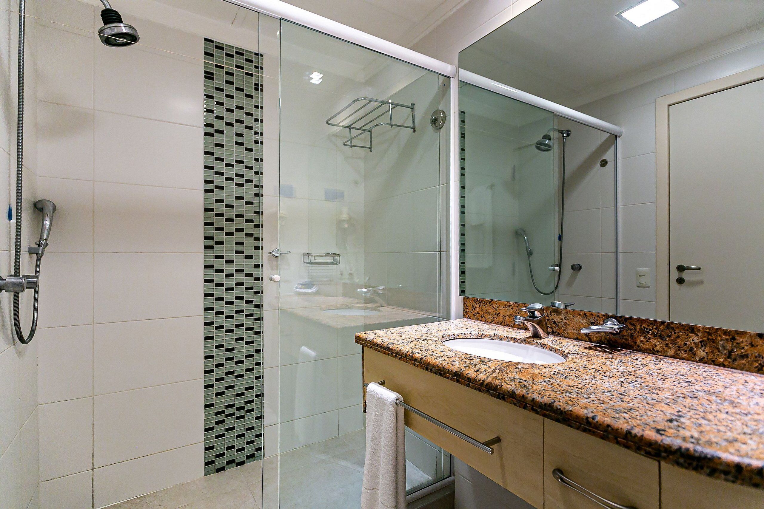 Une salle de bain moderne avec une douche à parois de verre, un lavabo sur un plan de travail en granit et un grand miroir.