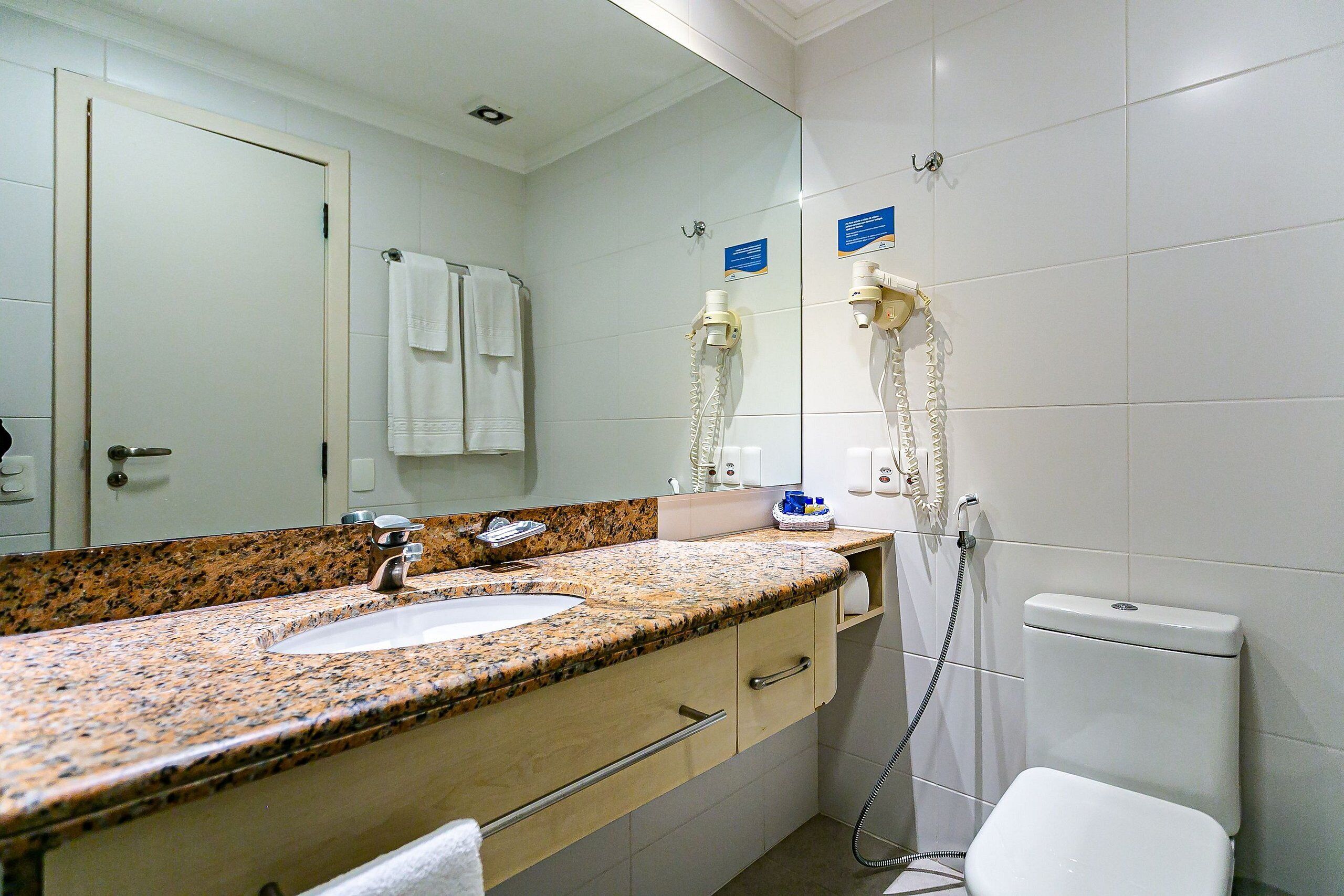 Et badeværelse med vask med granitbordplade, et spejl, et toilet og en bruser med brusehoved.