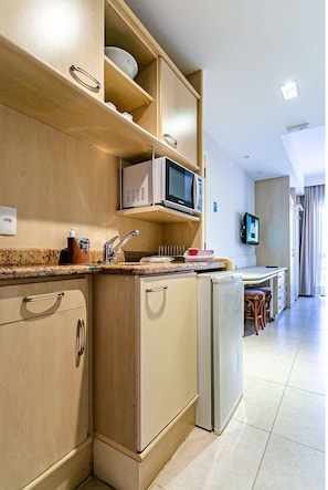 Een praktische keuken met een magnetron, een kleine koelkast en een spoelbak. Op de achtergrond is een eethoek met een tafel en stoelen te zien.