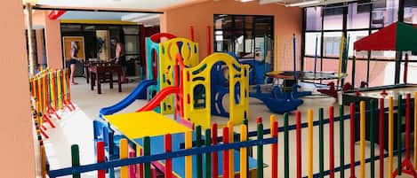 Zona de juegos infantiles con estructuras coloridas y una sección delimitada por una cerca.