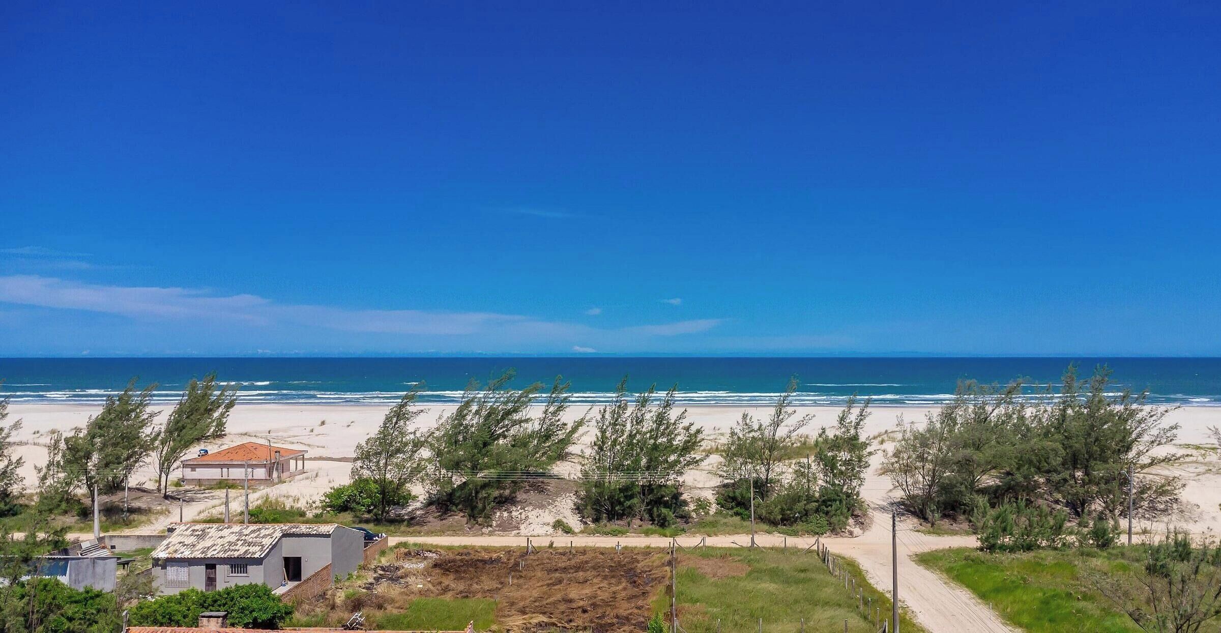 Vista costera con playa arenosa, cielo azul despejado y algunos edificios al frente.