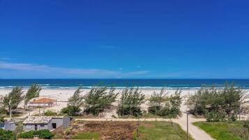 Vista costera con playa arenosa, cielo azul despejado y algunos edificios al frente.