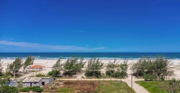 Vista costeira com uma praia arenosa, céu azul claro e alguns edifícios ao primeiro plano.