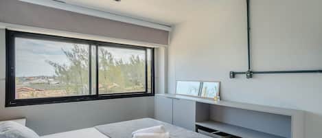 A modern bedroom with a large window, a bedside table with a towel, and a built-in shelf.
