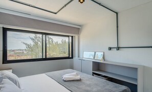 Un dormitorio moderno con un ventanal grande, una mesita de noche con una toalla y un estante empotrado.