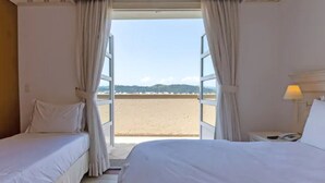 Een hotelkamer met twee bedden, een nachtkastje en uitzicht op het strand.