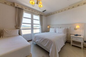 A hotel room with two beds, a large window with curtains, a bedside table with a lamp, and a view of the sea. - Exclusive Penthouse in a Luxury Resort Ilc4501 (Florianópolis)