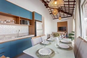 Una cocina moderna con armarios azules, una encimera blanca y un área de comedor preparada para cuatro personas, con una mesa de vidrio.
