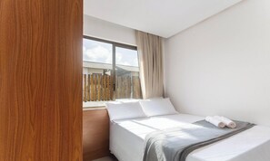 A bedroom with a bed, a window with curtains, and a view of a wooden fence outside. - 2-suite House by the Lagoon in Marau Cdl0008 (Maraú)