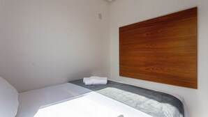 Un letto piccolo e ben rifatto con una testiera in legno in una stanza dallo stile minimalista.