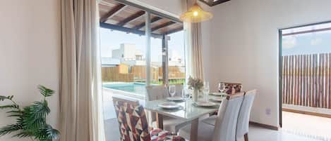 A dining area with a glass table, chairs, and a hanging light fixture.
