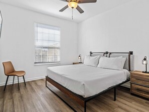 Ein Schlafzimmer mit Bett, Stuhl, Nachttisch, Lampe und Deckenventilator.