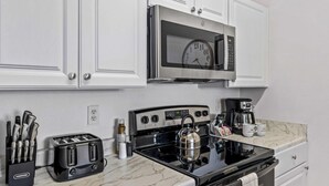 A kitchen with white cabinets, a stainless steel microwave, a black stove, a coffee maker, and a toaster. - Beautiful Condo at Windsor Palms Resort (Kissimmee)