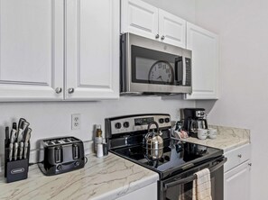 A kitchen with white cabinets, a stainless steel microwave, a black stove, a coffee maker, and a toaster. - Beautiful Condo at Windsor Palms Resort (Kissimmee)