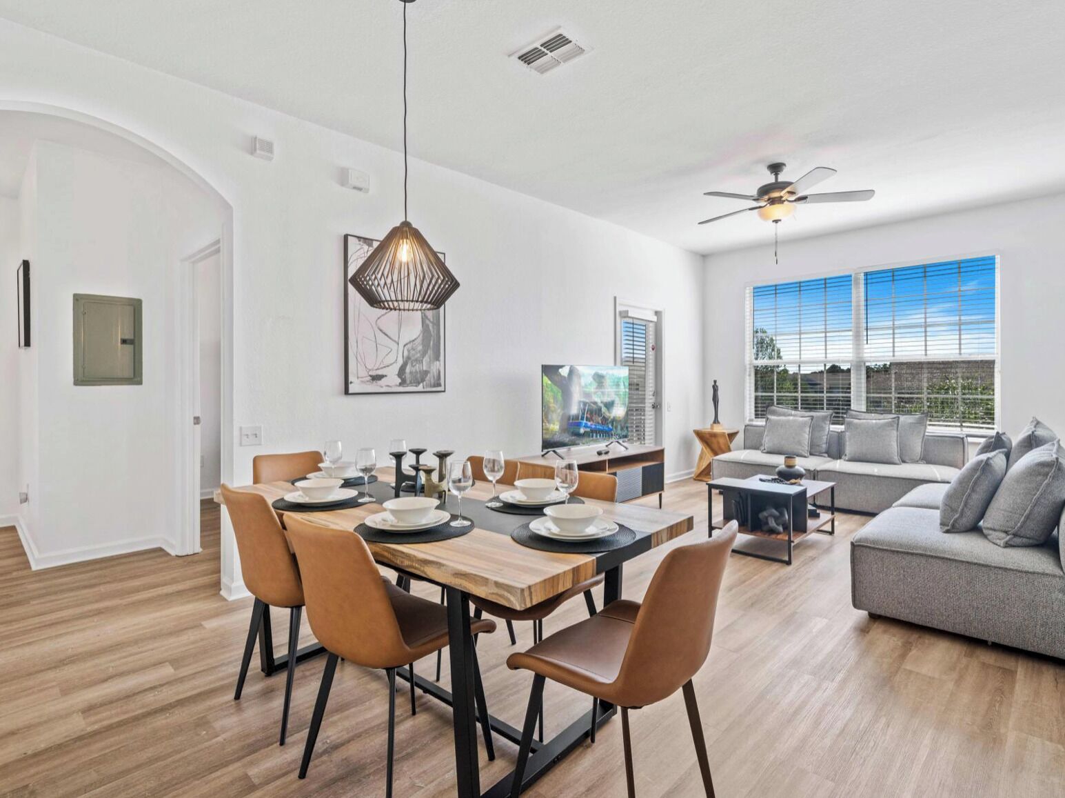 A modern living room with a dining area, a grey sofa, and a ceiling fan.