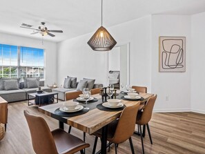 A modern living room with a dining area, a ceiling fan, and a dining table set for four. - Beautiful Condo at Windsor Palms Resort (Kissimmee)