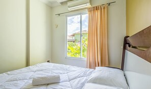 Ein Schlafzimmer mit Bett, Klimaanlage, einem Fenster mit Vorhängen und Blick auf Grünfläche.