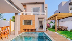 Ein modernes, zweistöckiges Haus mit Schwimmbad, Sitzgelegenheiten im Freien und einer überdachten Terrasse.