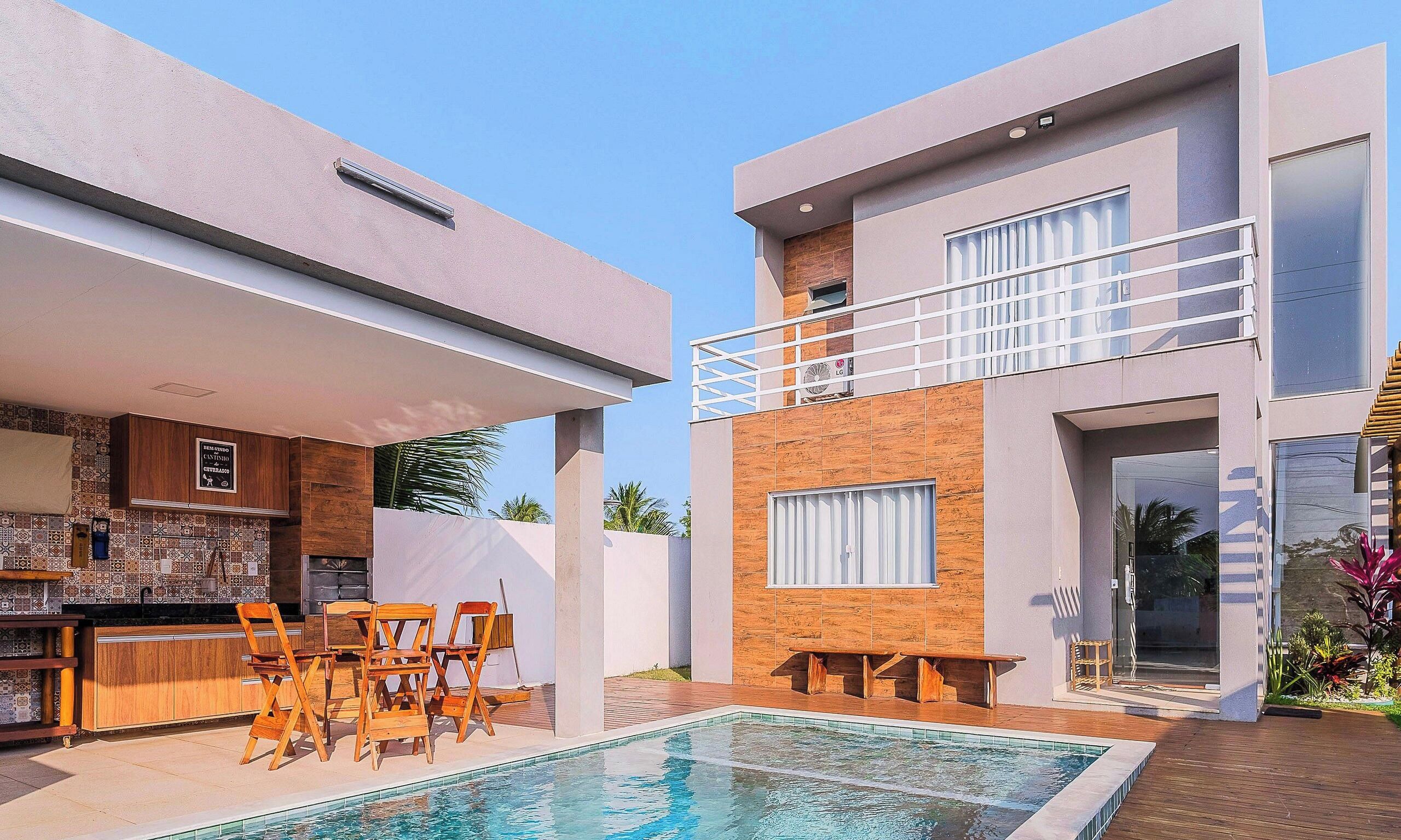 A modern two-story house with a swimming pool, wooden deck, and outdoor furniture.