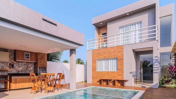 Ein modernes, zweistöckiges Haus mit Schwimmbad, Sitzgelegenheit im Freien und einem sichtbaren Küchenbereich.