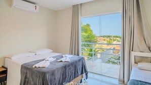 Ein Hotelzimmer mit Bett, einem Fenster mit Vorhängen, einem Balkon und einer Klimaanlage.
