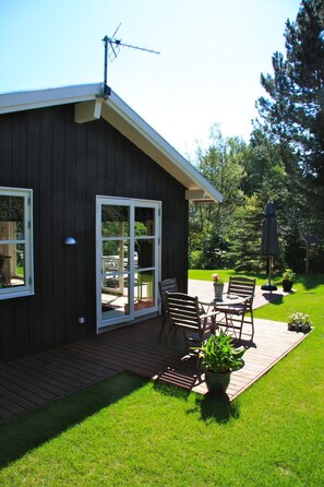 Une cabane en bois dotée d’une porte-fenêtre coulissante, d’une terrasse avec mobilier d’extérieur et d’une pelouse bien entretenue.