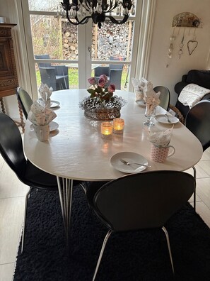 A dining table set for four with chairs, a chandelier, and a view of the outdoors. - Hyggeligt sommerhus ved Nykøbing Lyng (Nykøbing Sjælland)