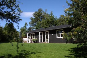 Ein zweistöckiges Haus mit dunkler Fassade, Fenstern mit weißen Rahmen und einer Veranda mit Tisch und Stühlen.