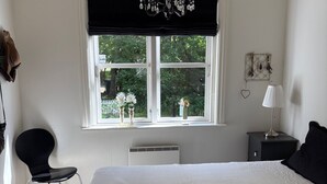 Una camera da letto con un letto grande, una finestra vista su vegetazione, una sedia, un comodino e una lampada.